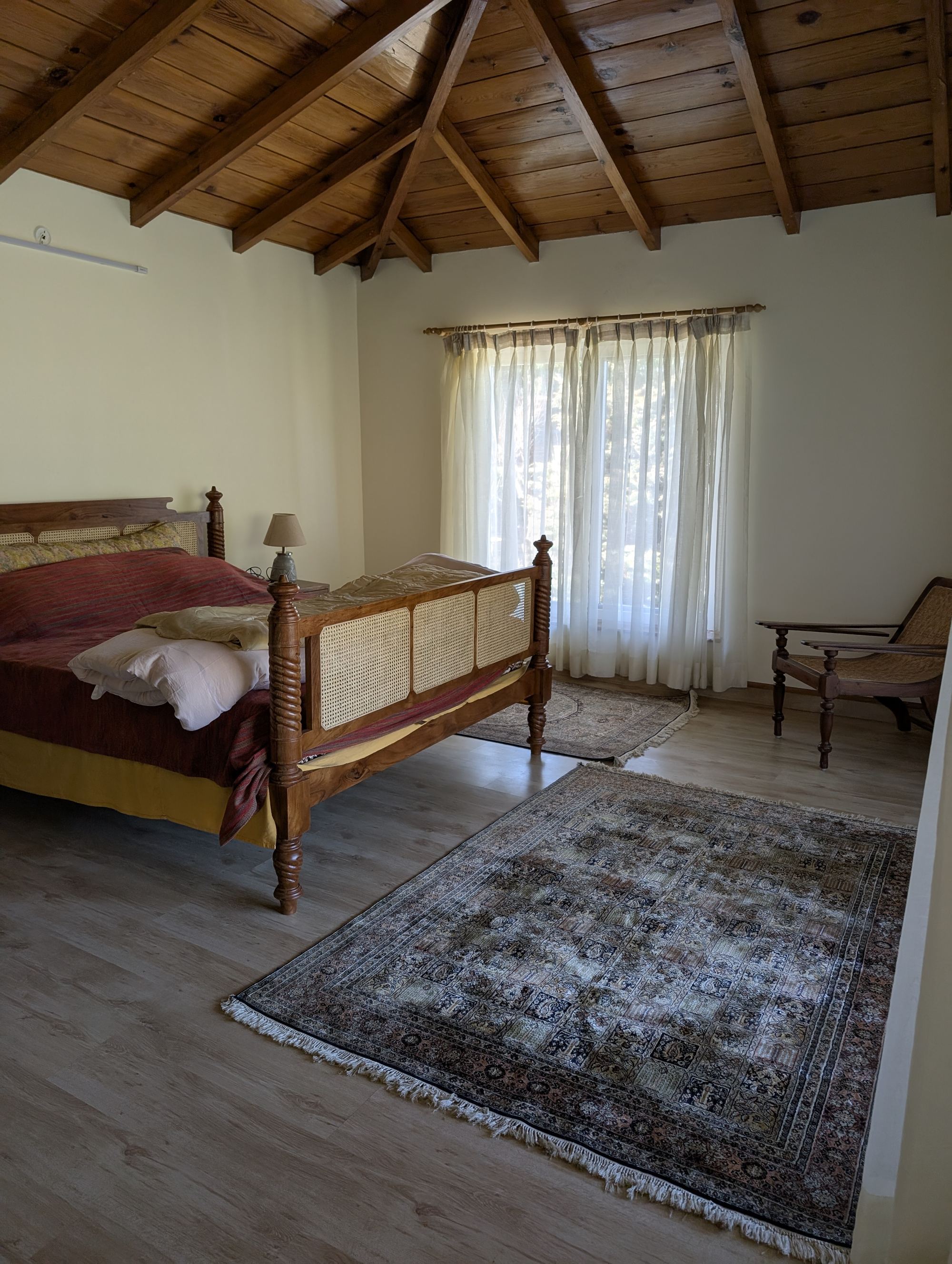 A bedroom with wood-beamed ceiling and cane furniture